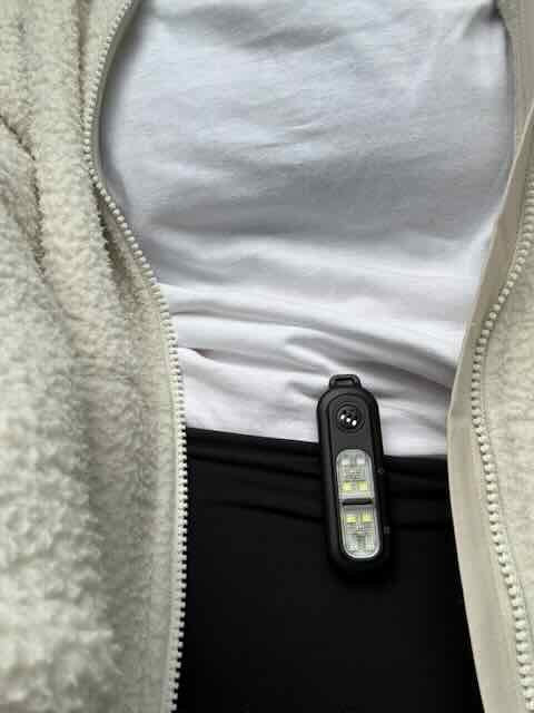 clip on personal safety alarm device attached to a person wearing a  fleece jacket.
