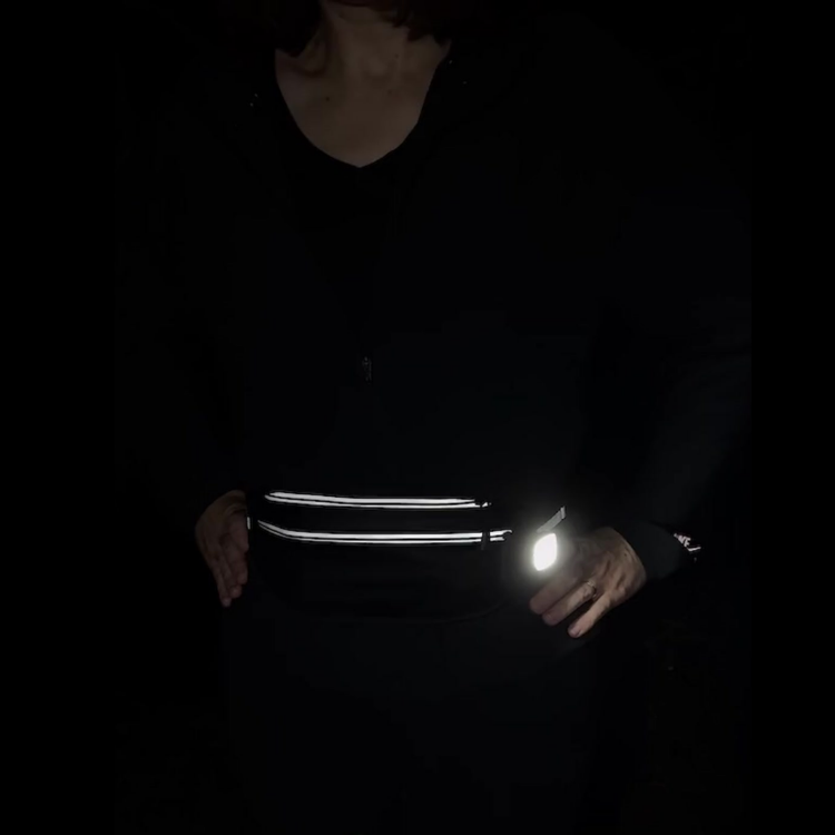Person wearing reflective walking bag with clip on light that is switched on.